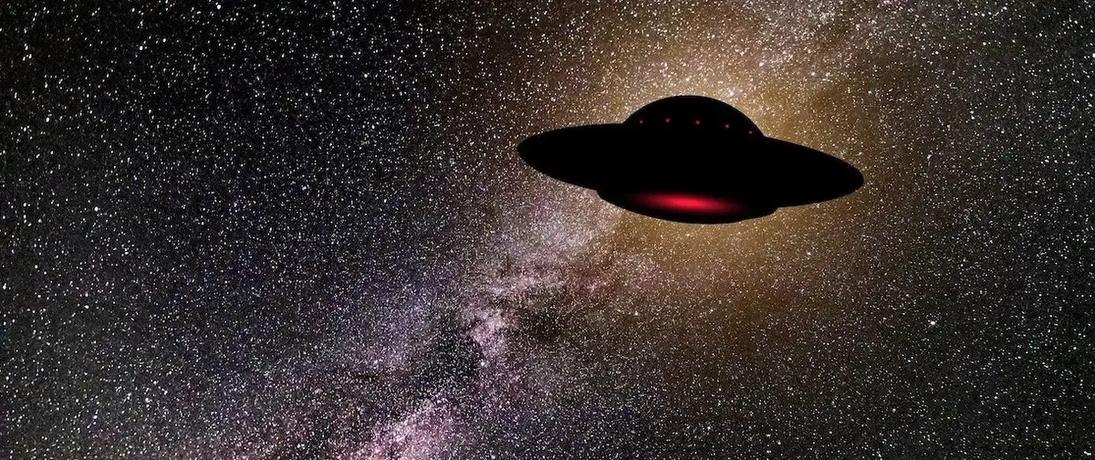 Silhouette of a flying saucer with red lights hovering against a starry night sky.