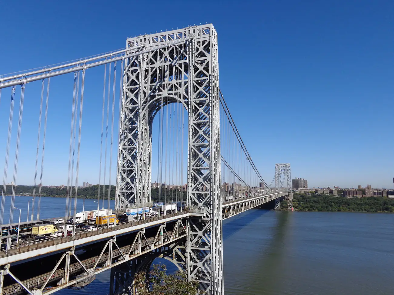 George Washington Bridge Steel suspension bridge with traffic, spanning a wide river under a clear blue sky.