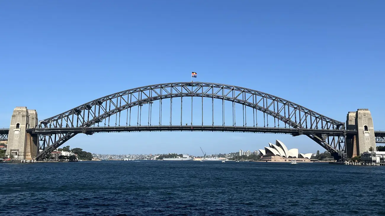 Sydney Harbour Bridge Sydney Harbour Bridge arches over blue water with the Opera House visible on the right under a clear sky.