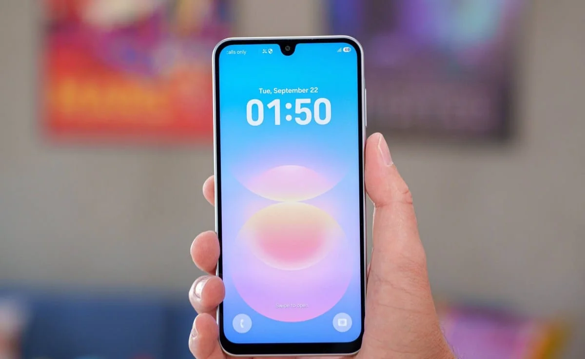 gsmarena_005 Hand holding a smartphone upright with a blue gradient wallpaper and the time 01:50 on the screen (lock screen).