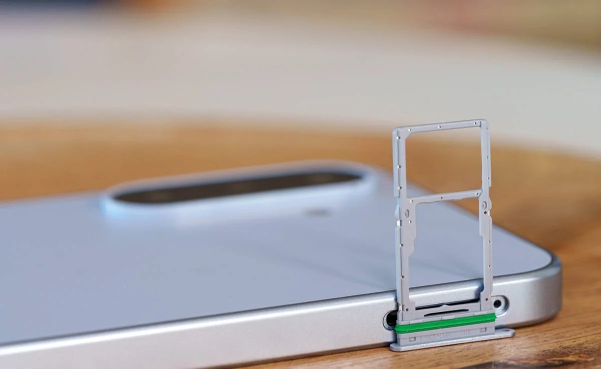 gsmarena_023 SIM card tray ejected from a silver smartphone lying on a wooden table surface