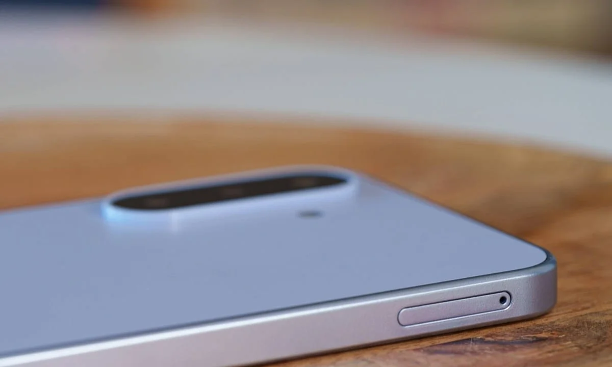 gsmarena_024 Close-up of a silver smartphone on a wooden table, highlighting its rounded dual-camera bump on the back.