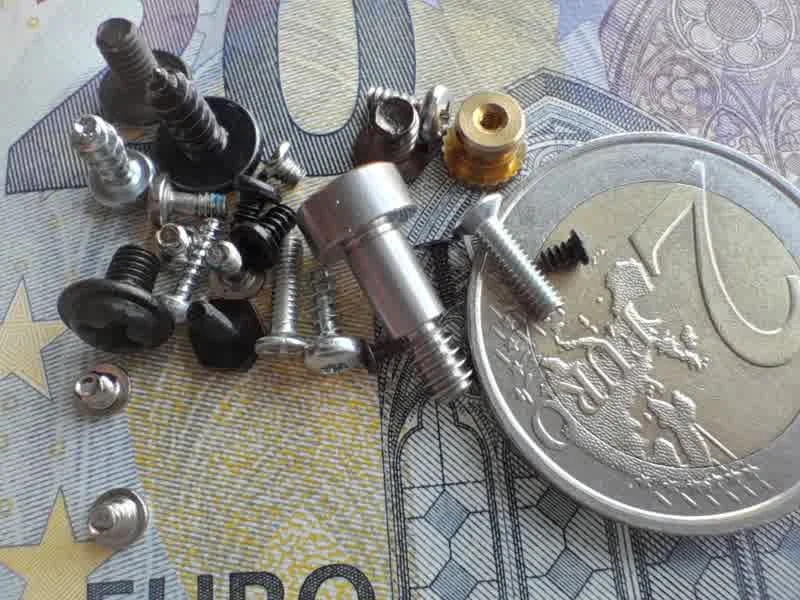 gsmarena_6101 Assorted screws, bolts, and fasteners scattered on a 1-euro coin and euro banknote for scale.